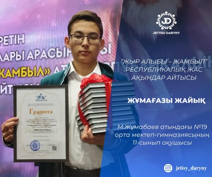На фото изображён ученик Жумагазы Жаик, победивший в республиканском айтысе юных акынов под названием «Жыр алыбы – Жамбыл». Он является учеником 11 класса средней школы-гимназии №19 имени М.Жумабаева. В руках у него грамота и стопка книг, перевязанная красной лентой. На фоне — большой экран с названием мероприятия. В правом верхнем углу — логотип «Jetysu Daryny». В правом нижнем углу указан Instagram-аккаунт @jetisy_daryny.